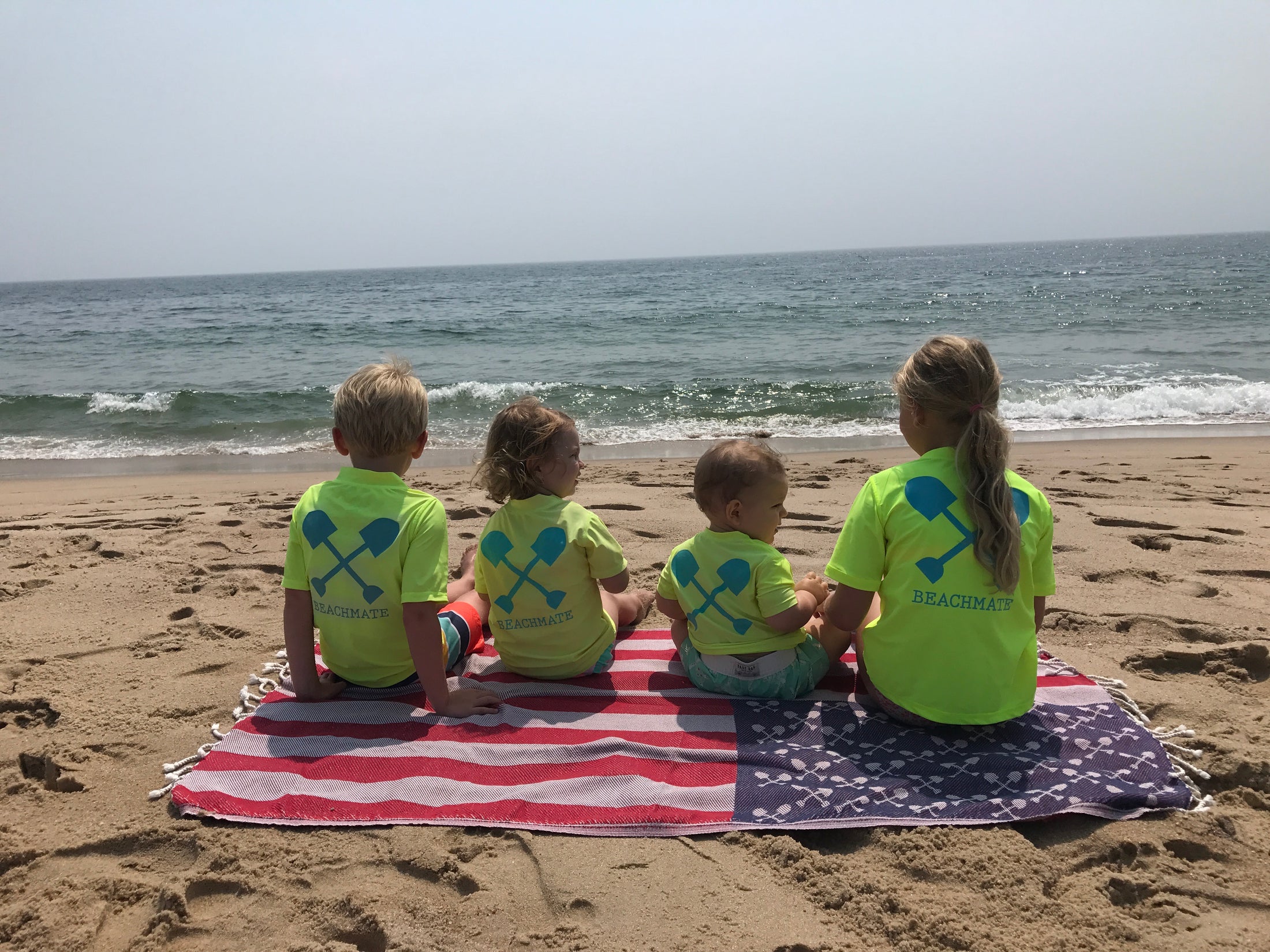 Group of kids in bright Beachmate short‑sleeve rash guards sitting on the beach