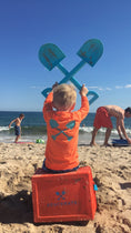 Load image into Gallery viewer, Child in orange long‑sleeve rash guard with sun hat holding a shovel at the beach