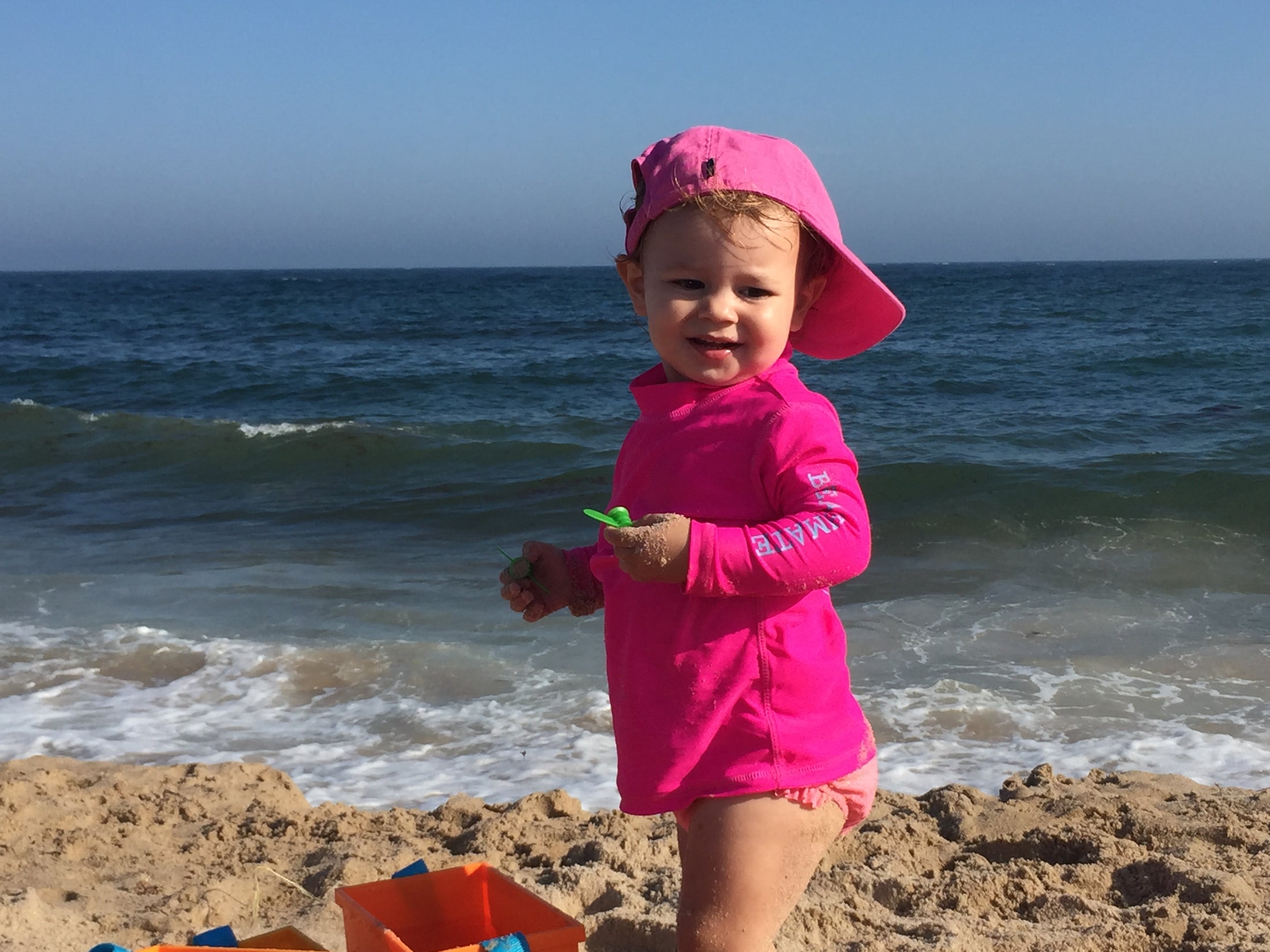 Girl wearing pink Beachmate long‑sleeve UPF 50 rash guard by the shoreline