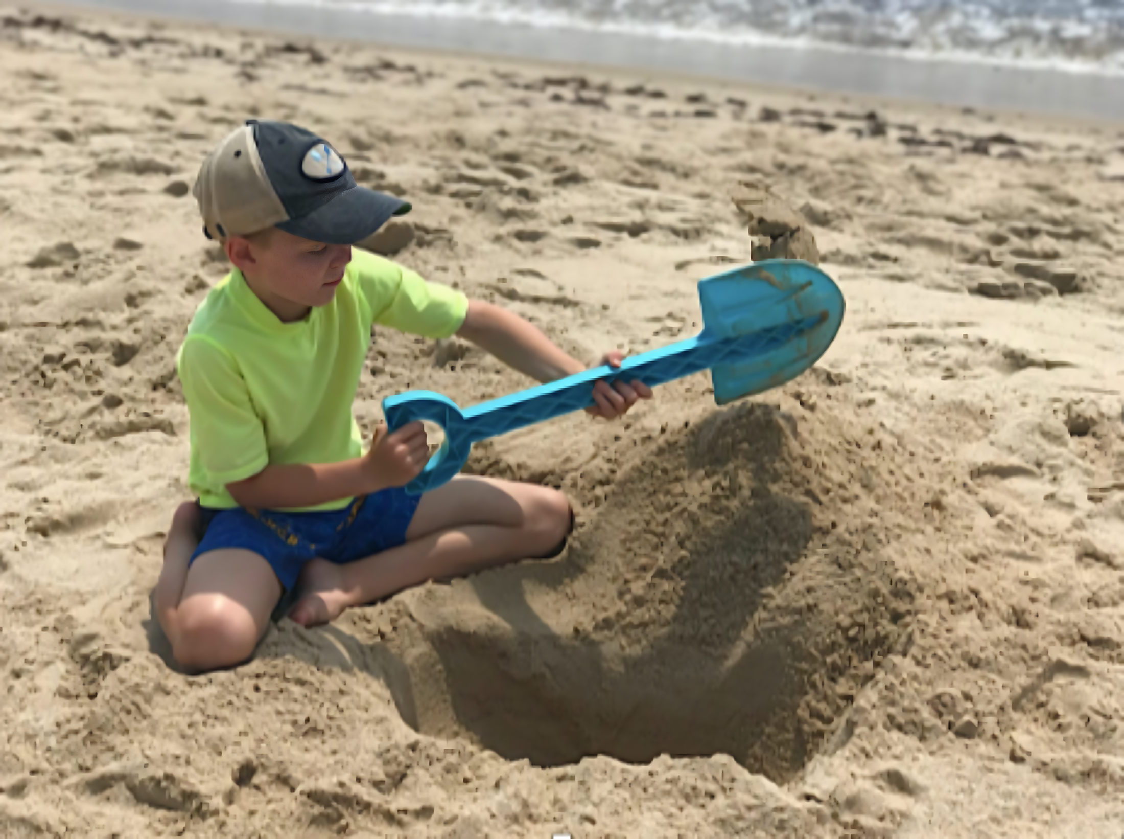 Child playing on a sandy beach with a  blue beachmate shovel