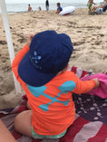 Load image into Gallery viewer, Toddler in orange Beachmate UPF 50 long‑sleeve rash guard sitting on the sand