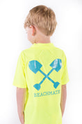 Load image into Gallery viewer, Child wearing neon yellow Beachmate short‑sleeve UPF 50 rash guard with crossed‑shovels logo on back