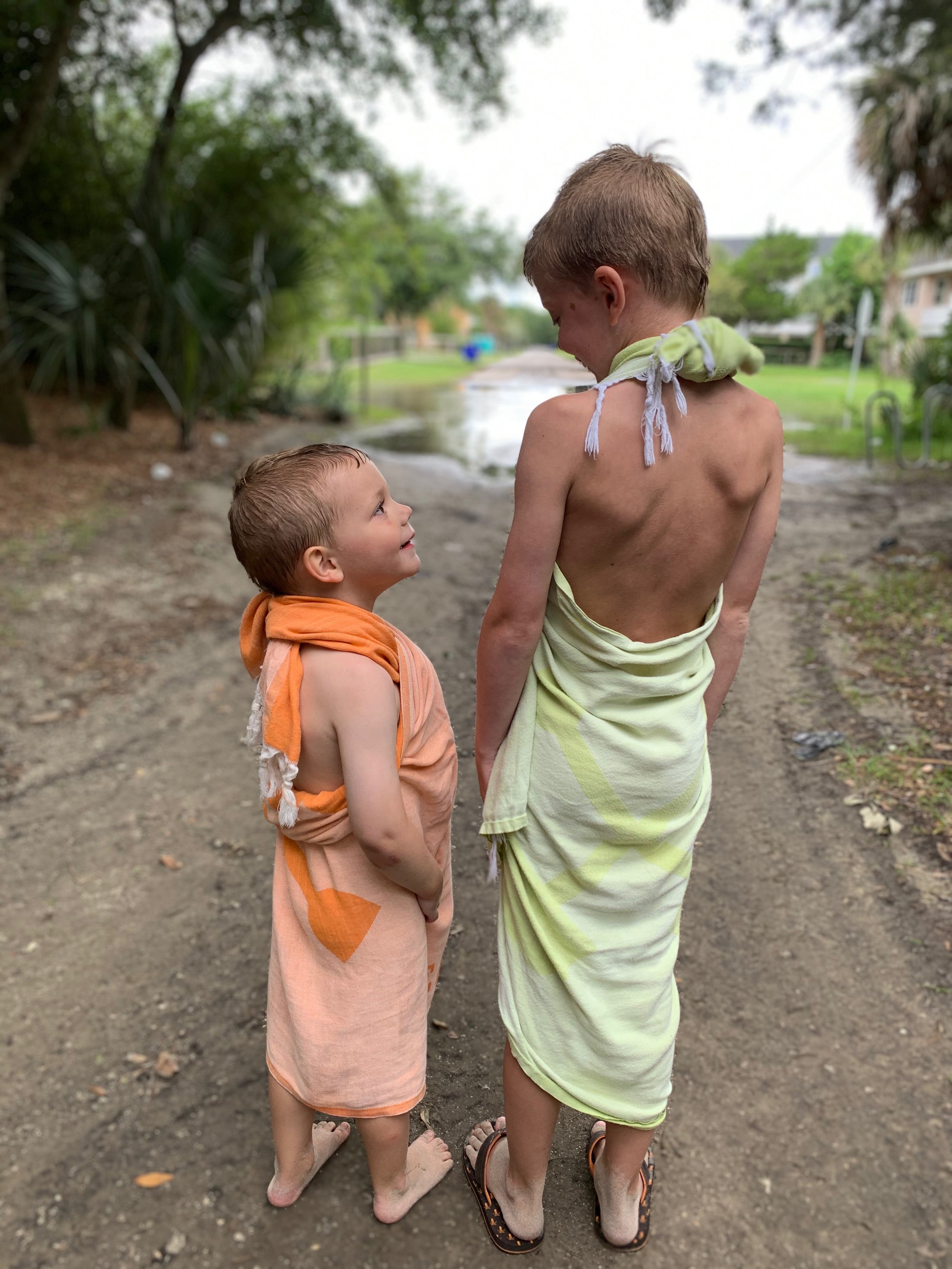 Lifestyle photo of children at the beach wrapped in Turkish towels, including orange