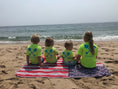 Load image into Gallery viewer, Group of kids in bright Beachmate short‑sleeve rash guards sitting on the beach
