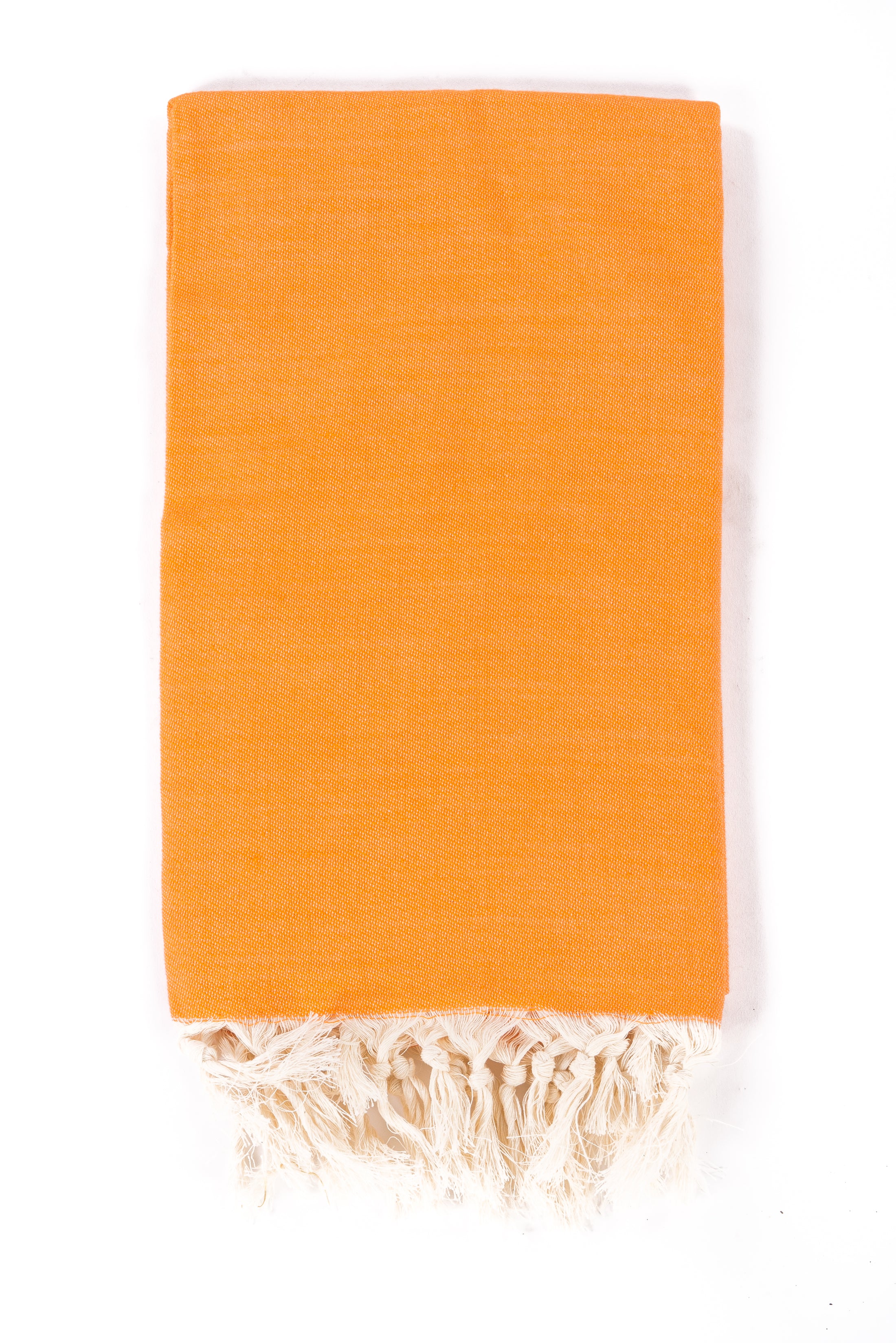 Folded orange Turkish towel with tassel fringe, studio view