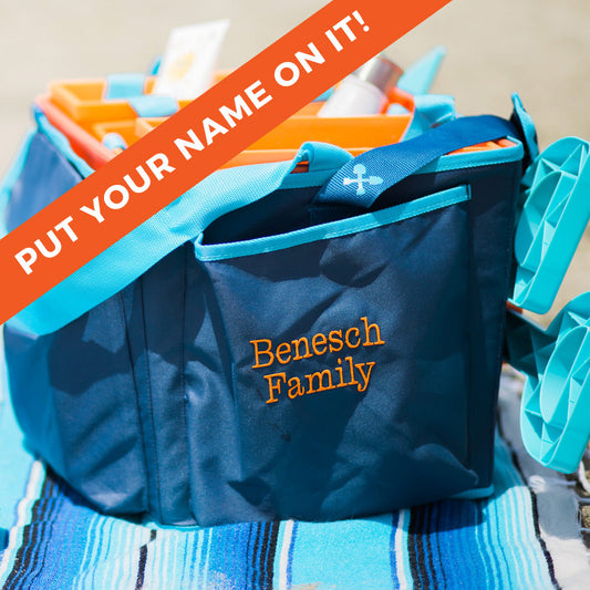 A blue and orange Beachmate tote bag with 'Benesch Family' customized in orange embroidery on the side, presented at a beach setting.